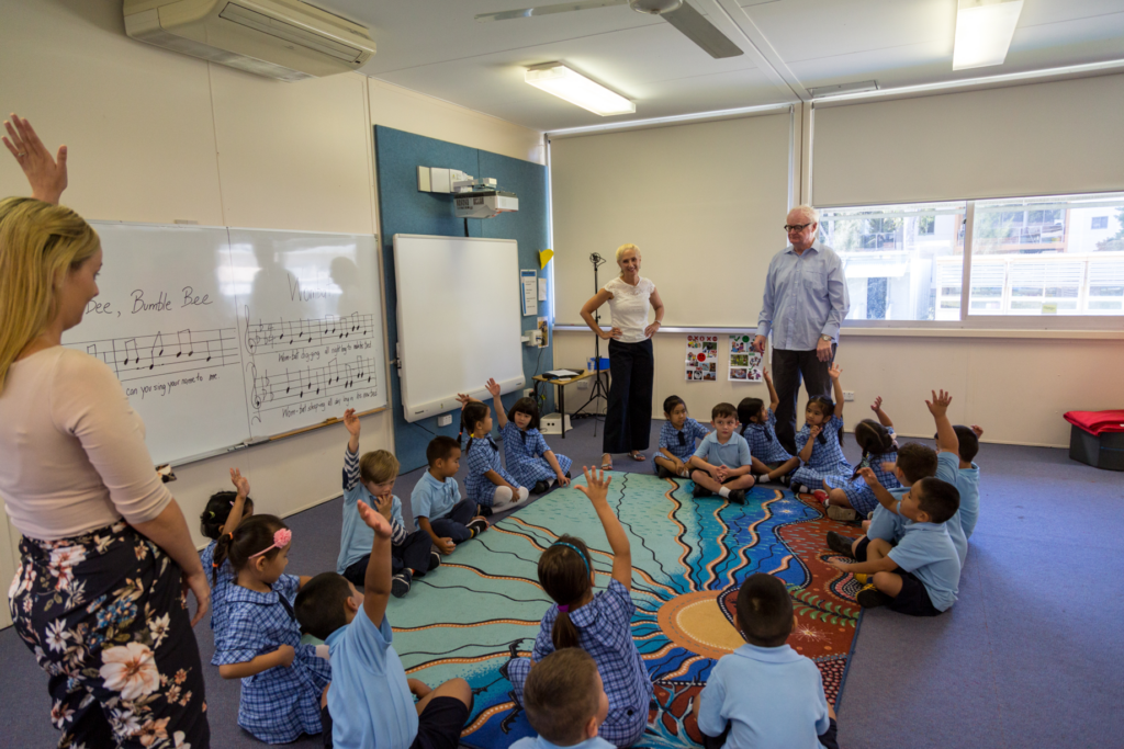 A classroom of primary school students sitting on the floor, with two music teacher mentors.