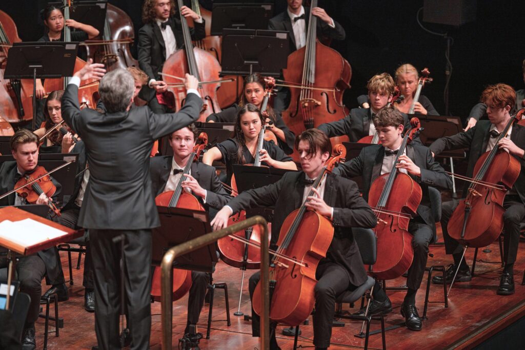 An orchestra of young musicians perform on stage.