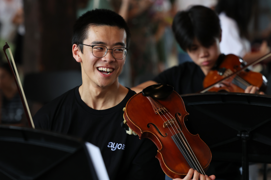 A young violinist wearing an AYO t-shift smiles during a rehearsal.