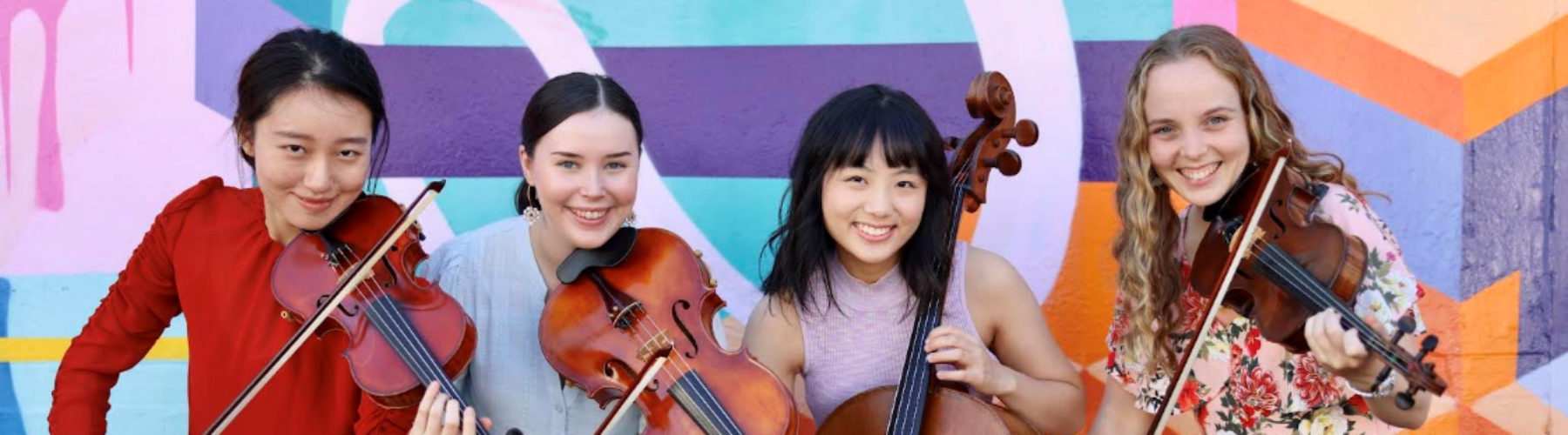 A quartet of string players smile at the camera in front of a colourful abstract mural