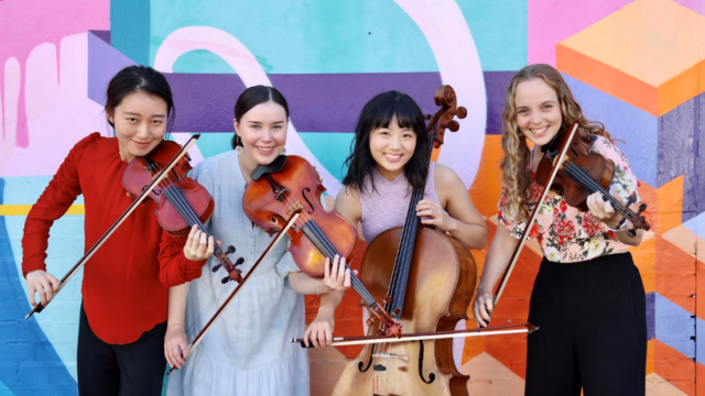 A quartet of string players smile at the camera in front of a colourful abstract mural