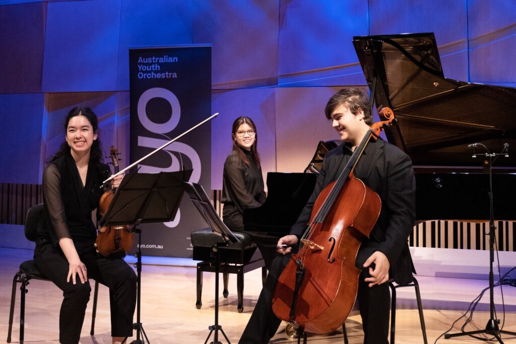 A piano trio chamber group laughs while they rehearse.