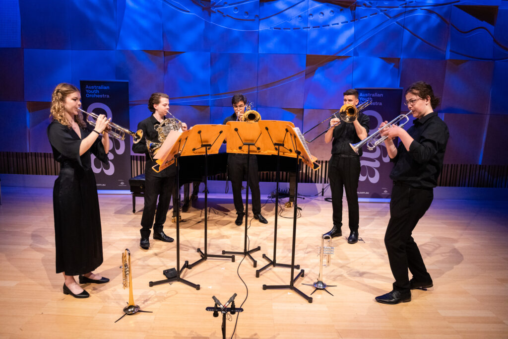 A brass quintet rehearses in a small chamber venue.