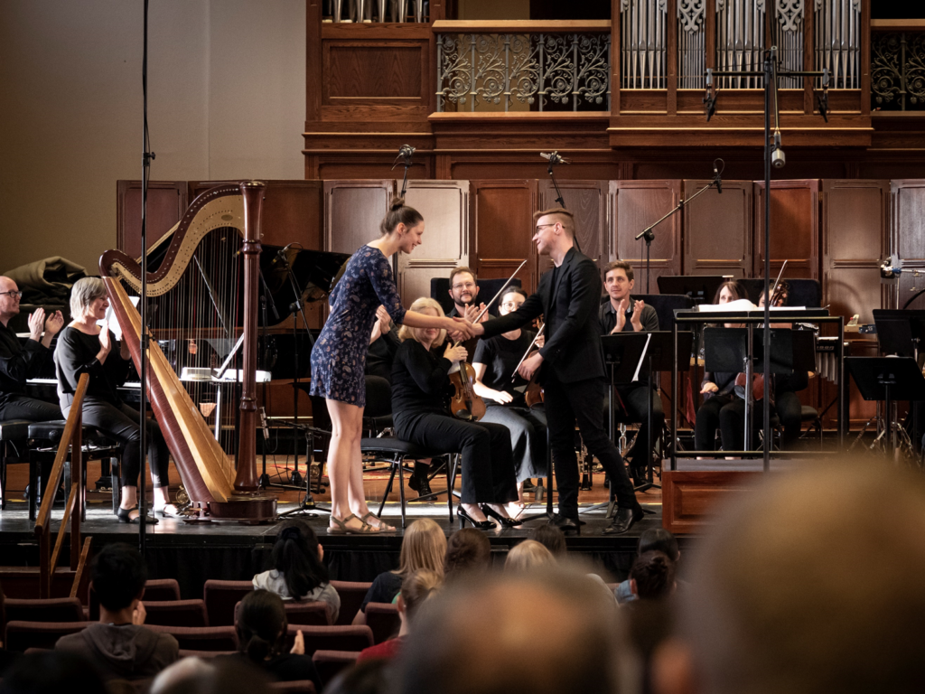 AYO composer Claire Farrell shakes the conductor's hand on stage during AYO National Music Camp 2020.
