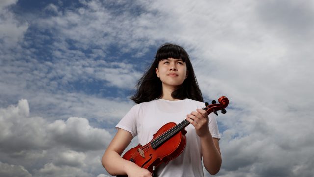 Young Girl with a white tshirt holding a violin with sky in the background