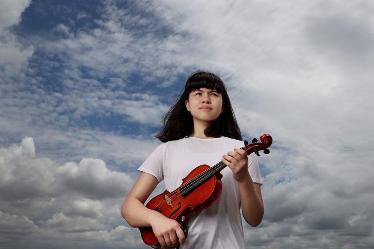 Young Girl with a white tshirt holding a violin with sky in the background