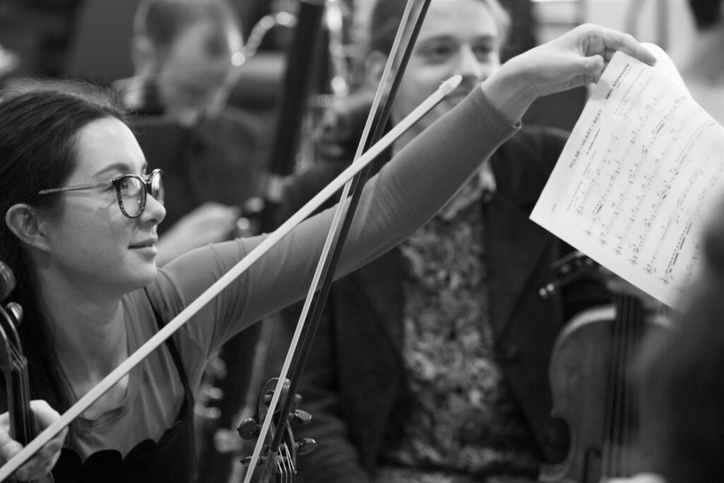 AYO violinist Emily Beauchamp reaches forward to her music stand during a rehearsal.