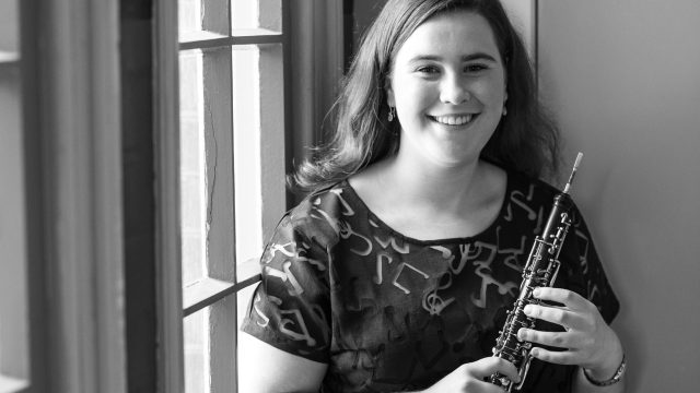 2021 Words About Music participant Emily Dodd holds her Oboe and smiles at the camera.