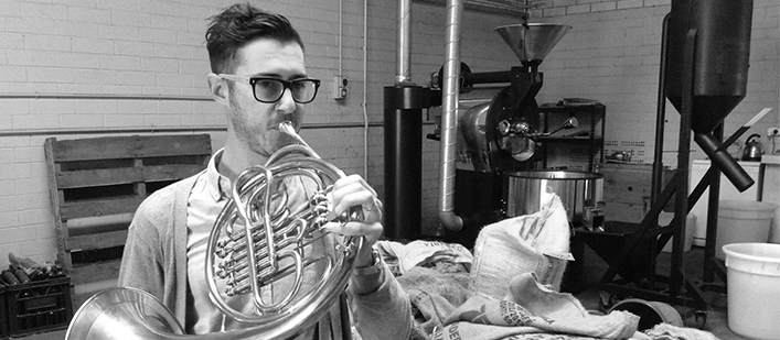 Greyscale image of AYO French Horn player Francesco Lo Surdo practising on his instrument.