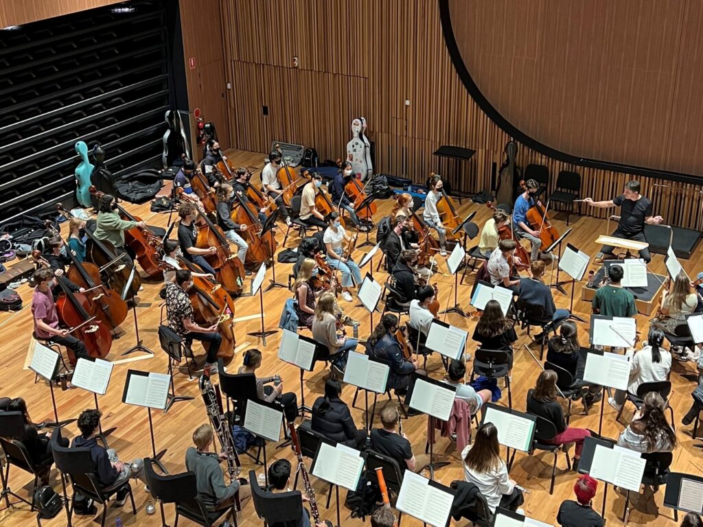 A bird's eye view of an AYO's Alexander Orchestra rehearsing in a large auditorium.