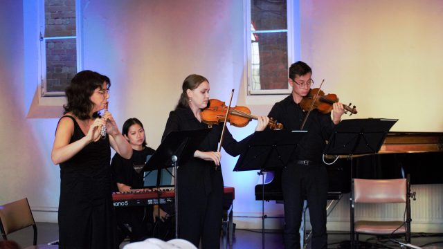 A chamber ensemble of young musicians in concert blacks perform in a former church.