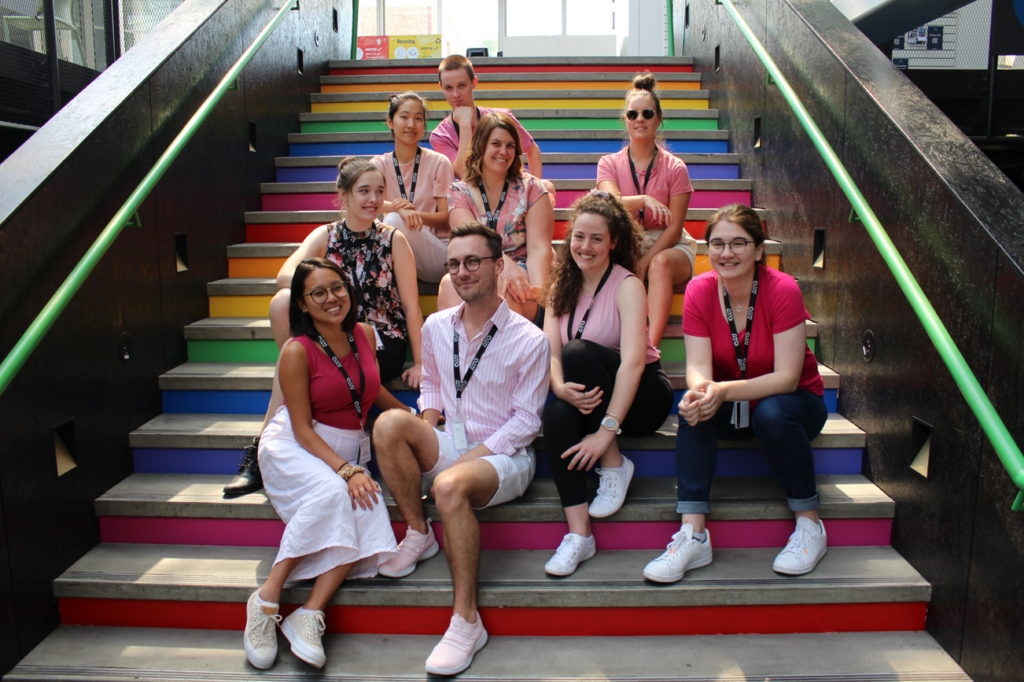 The Orchestral Management cohort from AYO National Music Camp 2020 sit in a group on a colourful flight of outdoor stairs. They are smiling at the camera.