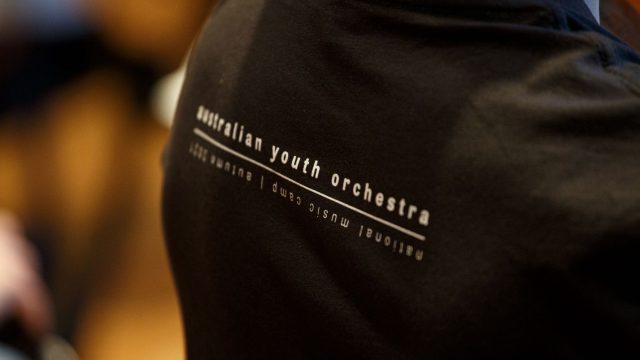 Close up of a black tshirt with the words 'Australian Youth Orchestra' in white writing on the back.