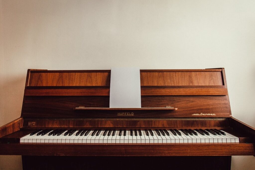 A wooden Hupfeld piano sits against a white wall.