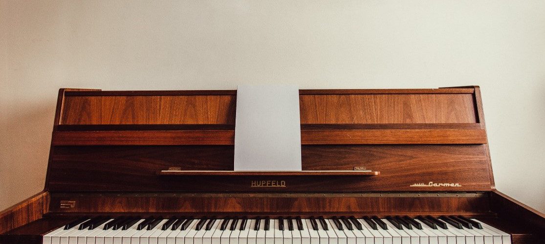 A wooden Hupfeld piano sits against a white wall.