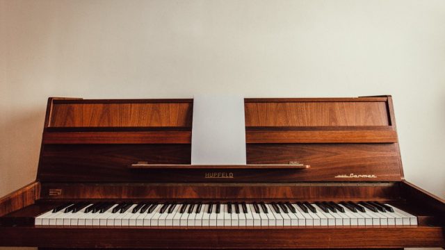 A wooden Hupfeld piano sits against a white wall.