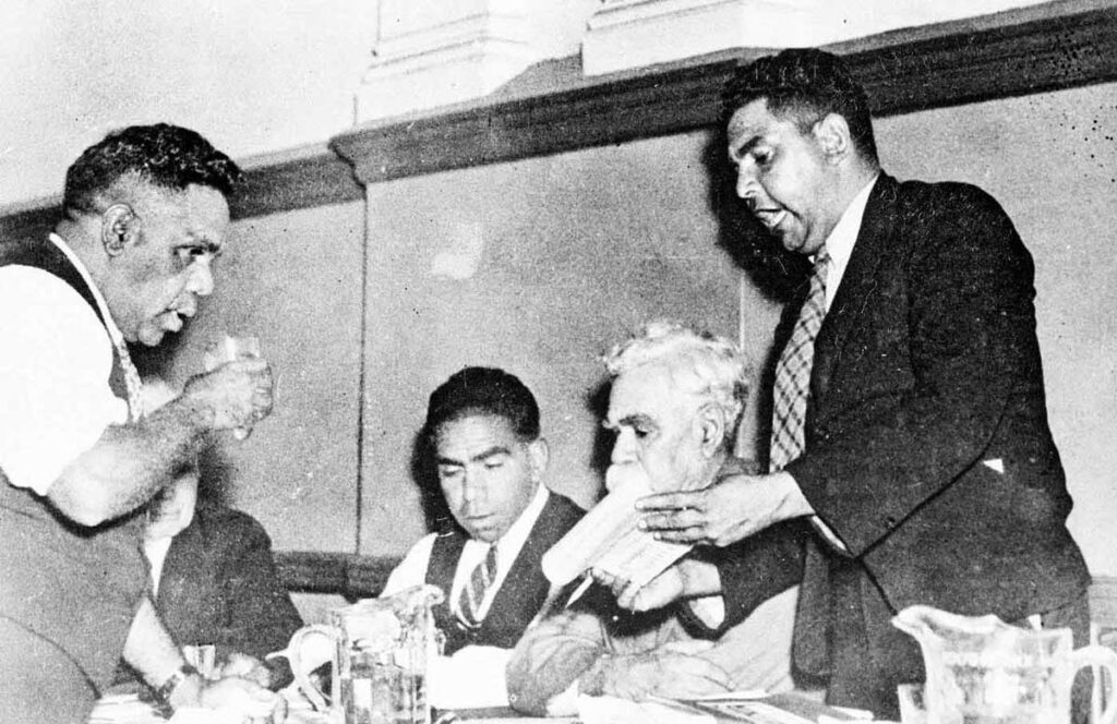 Black and white photo of four Aboriginal men seated at a table. From left to right: Tom Foster, Jack Kinchela, Douglas Nicholls, William Cooper, John Patten 