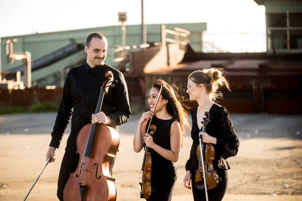 Three young musicians laugh as they hold their instruments,