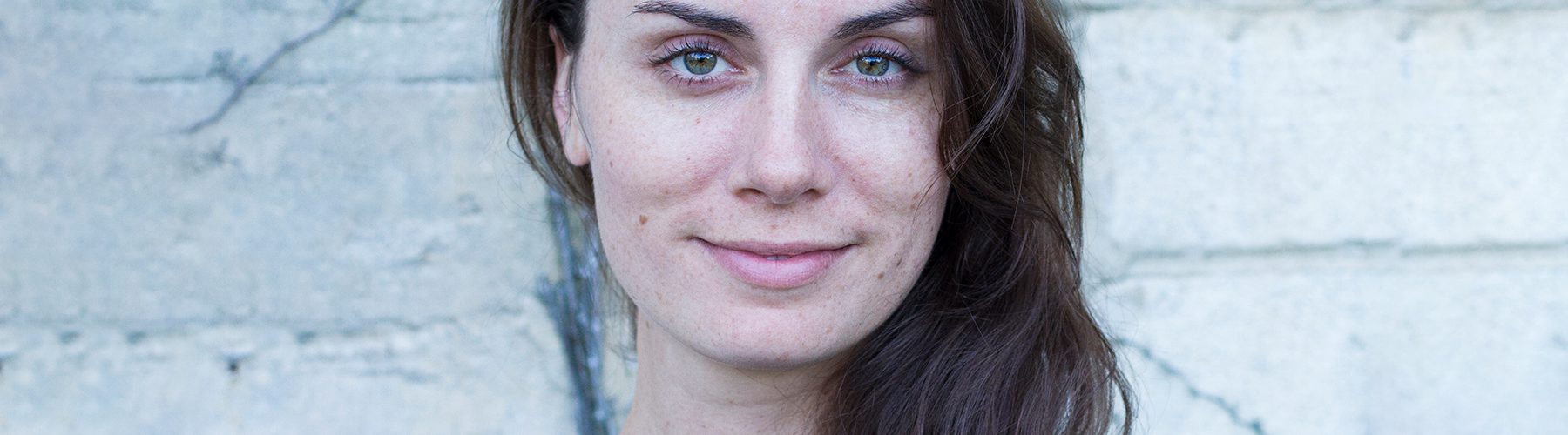 Composer Melody Eötvös smiles at the camera. She is wearing a blue top and has long brown hair.