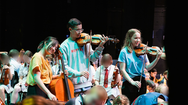 A group of musicians and school students perform on stage.