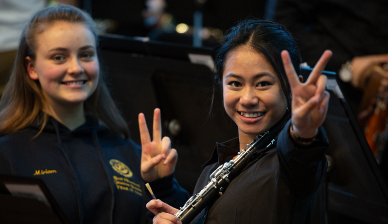 Two young musicians smile at the camera while making peace signs.