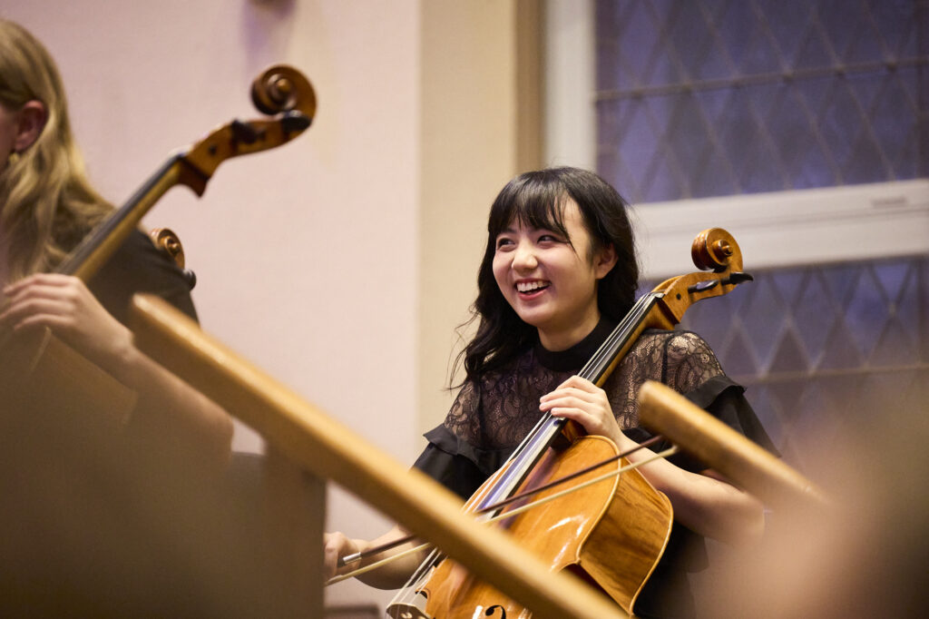 A young cellist smiles as she performs on stage.