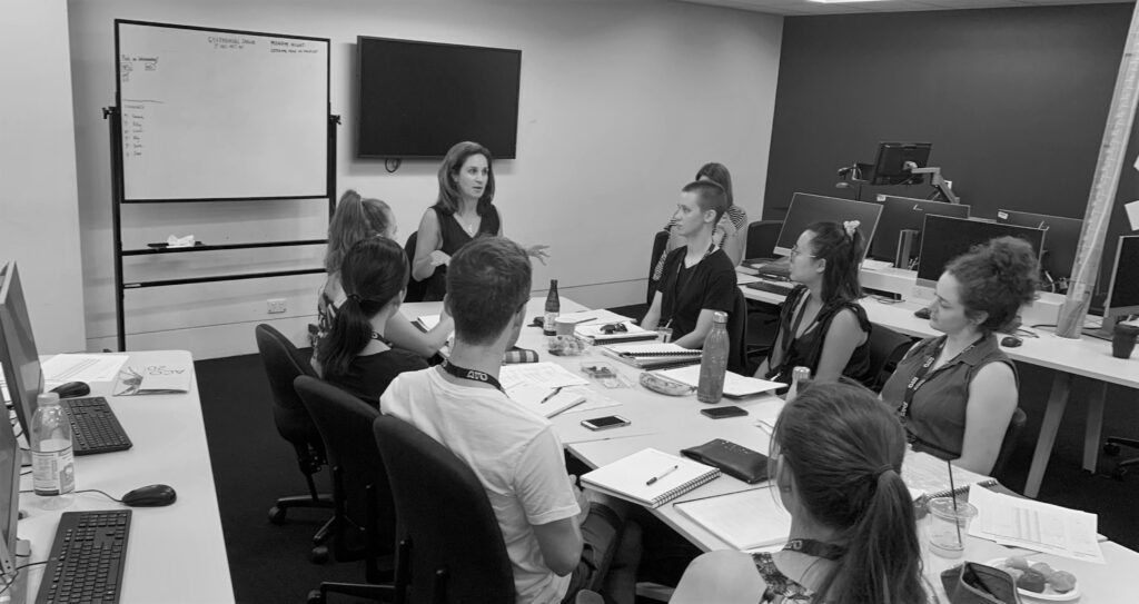 The Orchestral Management cohort from AYO National Music Camp 2020 sit around a table as they listen to a guest presenter.