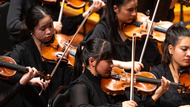 A photo of a group of violinists playing in an orchestra.