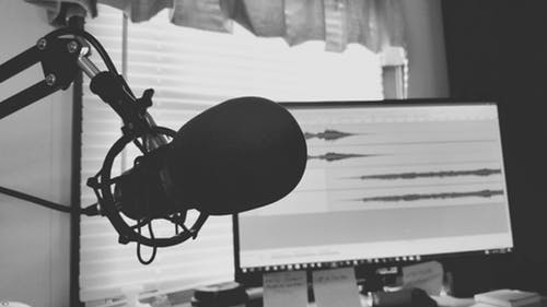 A greyscale image of a microphone on a stand and a computer processing an audio file.