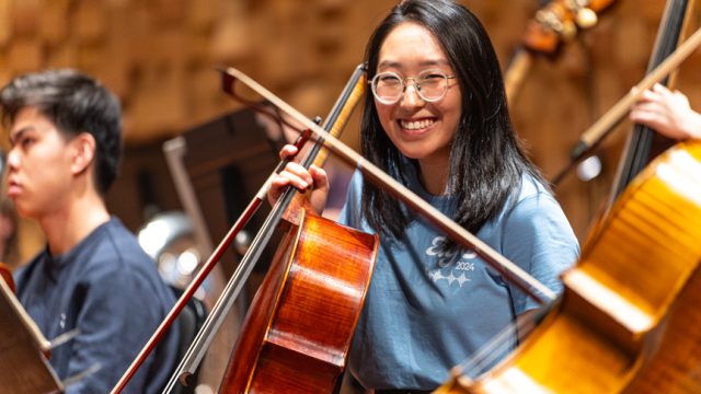 A photo of a young cellist smiling at the camera.