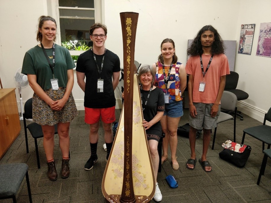 4 participants of AYO National Music Camp 2019 stand around a harpist seated with her instrument. They are all smiling.