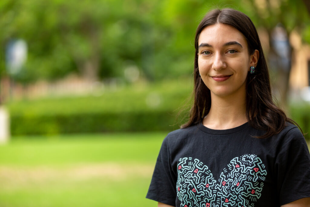 Singer and Words About Music participant Stella Joseph-Jarecki smiles at the camera. She is outside and surrounded by lush green plants,