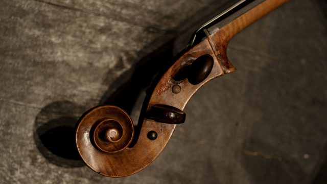 The top of a violin pictured centre on a dimly lit surface.