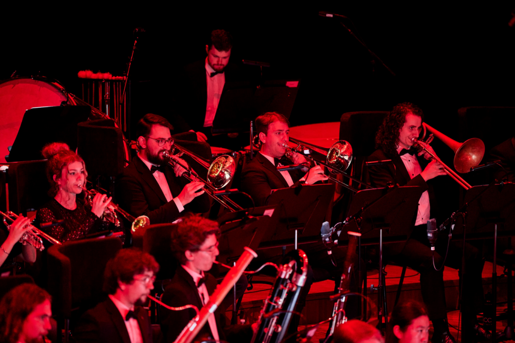 An orchestra of young musicians perform on stage, lit in red light.