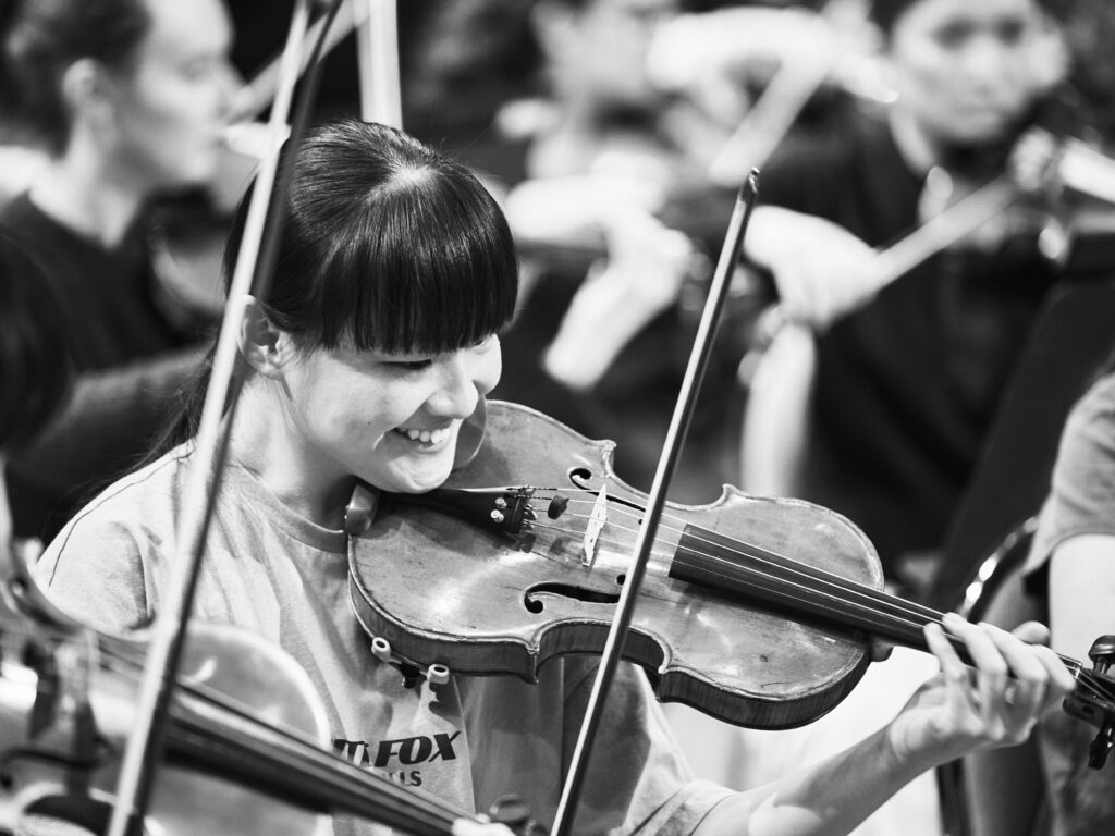 A black and white image of a young violinist smiling during rehearsal.