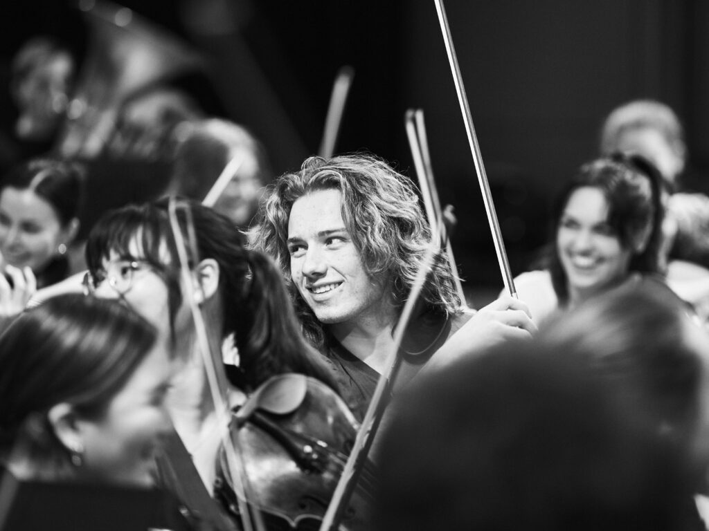 A black and white image of a young violinist smiling during rehearsal.