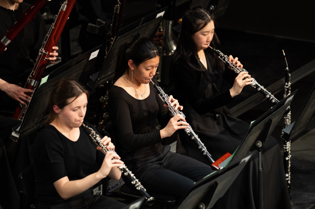 Three young oboists perform during a performance.