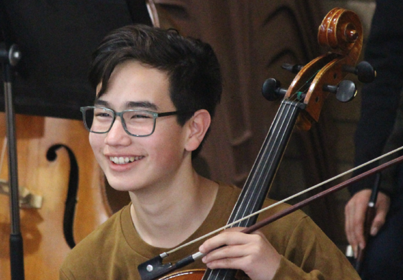 A young cellist smiles during an orchestra rehearsal.