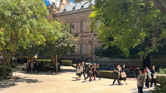 Young people dressed in concert blacks walk across a sunny courtyard.