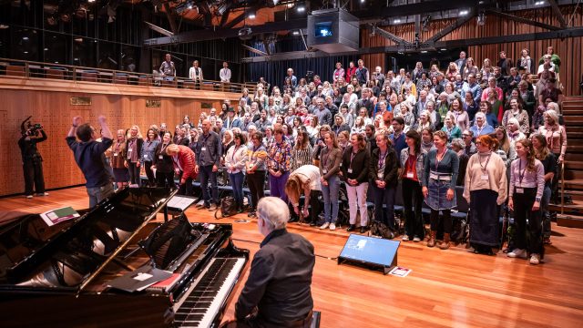 A group of people in a conference hall stand up to sing.