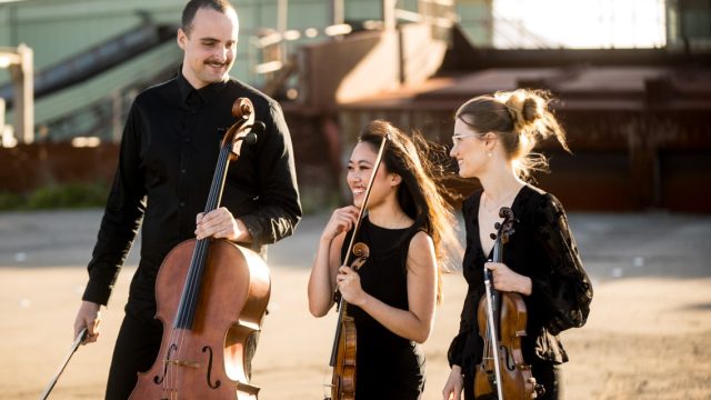 Three young musicians laugh as they hold their instruments,