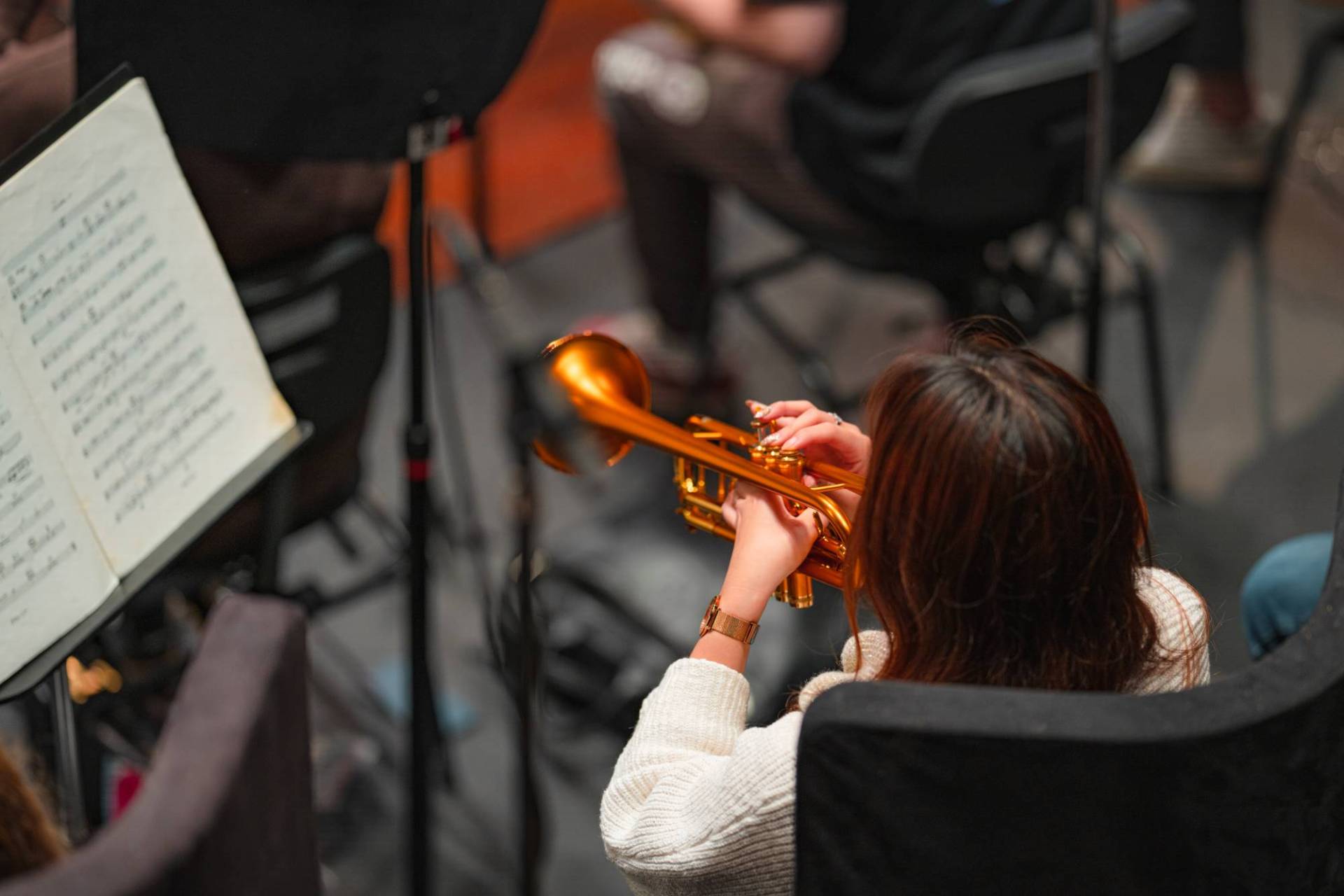 A trumpet player from the Australian Youth Orchestra rehearses at Perth Concert Hall. She is wearing a white long sleeve jumper with a gold watch and trumpet. Edify Media 2023