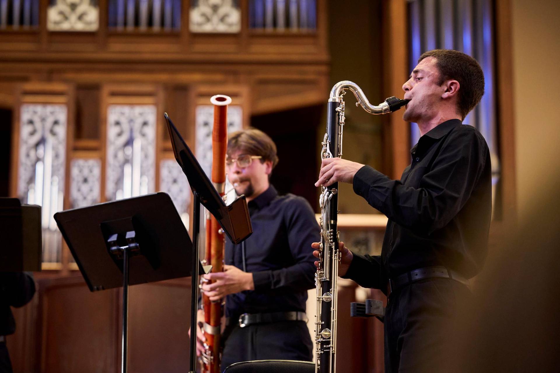 Musicians at the AYO National Music Camp play on stage in front of an organ. They are paying a bassoon and a bass clarinet, and wearing concert blacks. Claudio Raschella 2023