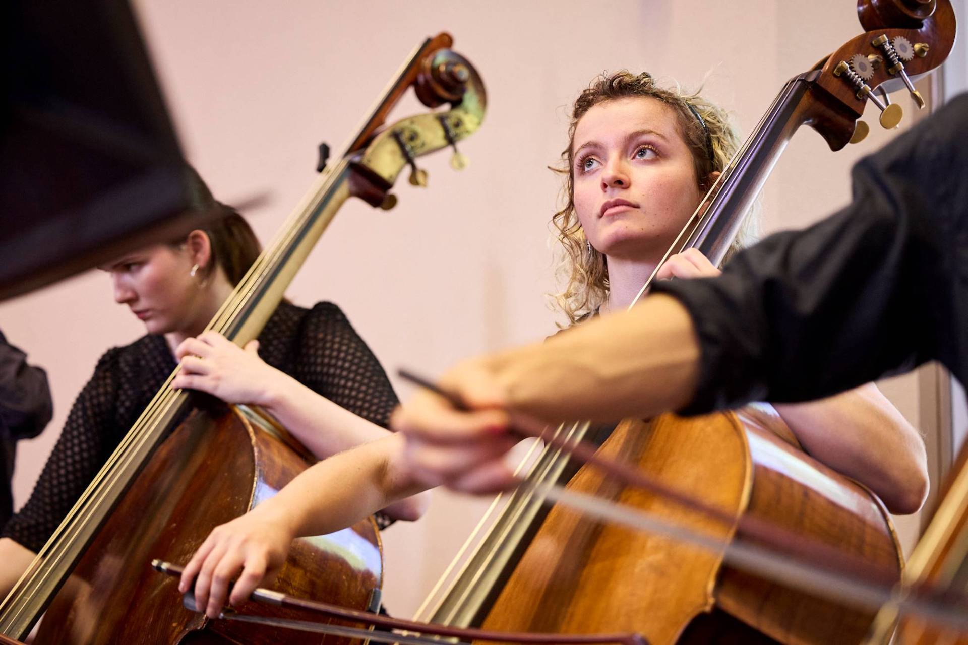 A cellist of the Australian Youth Orchestra looks up whilst playing at AYO National Music Camp. She has curly blond hair and is wearing concert blacks. Credit: Claudio Raschella 2023