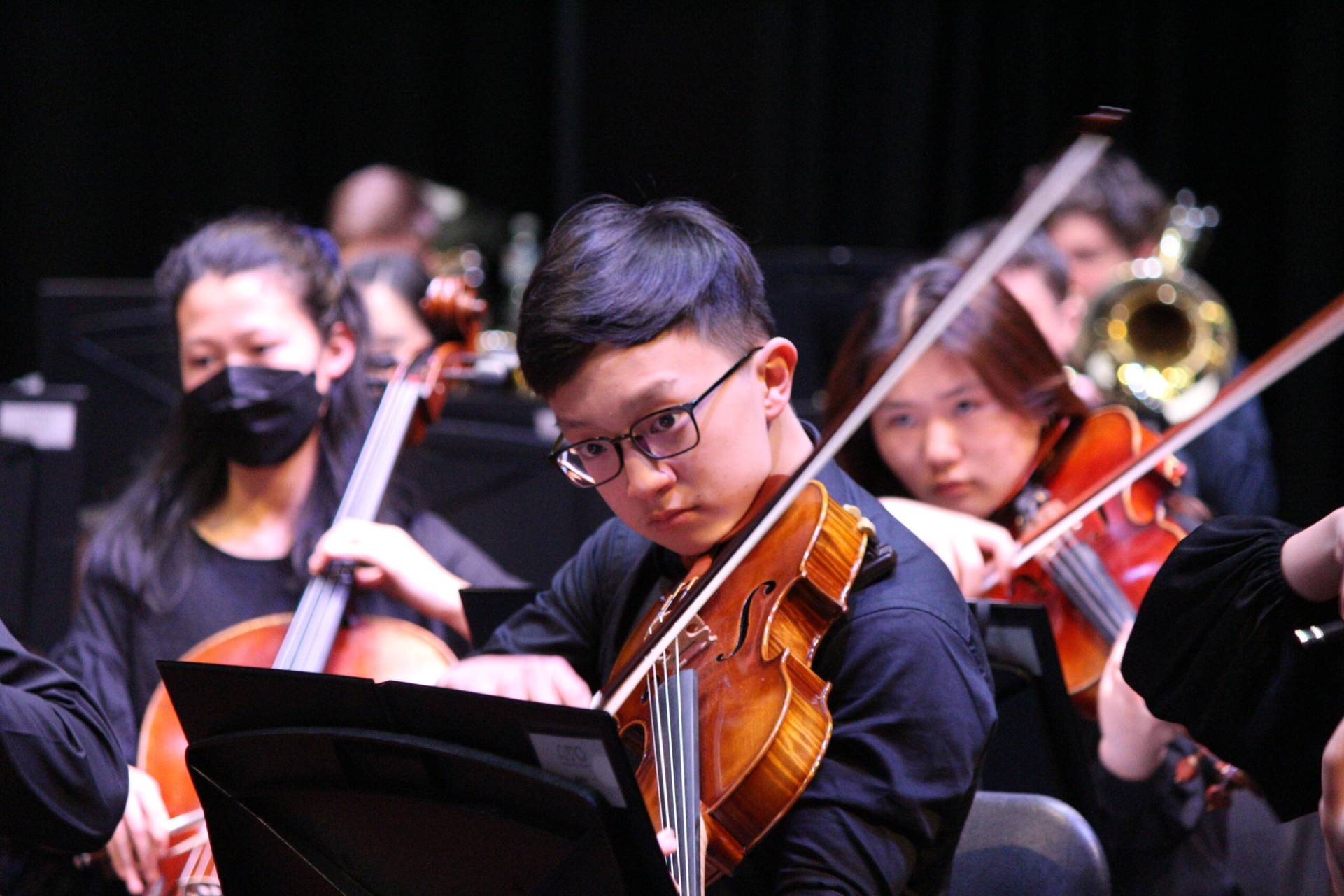 Young violinist performing with other musicians playing in the background out of focus.
